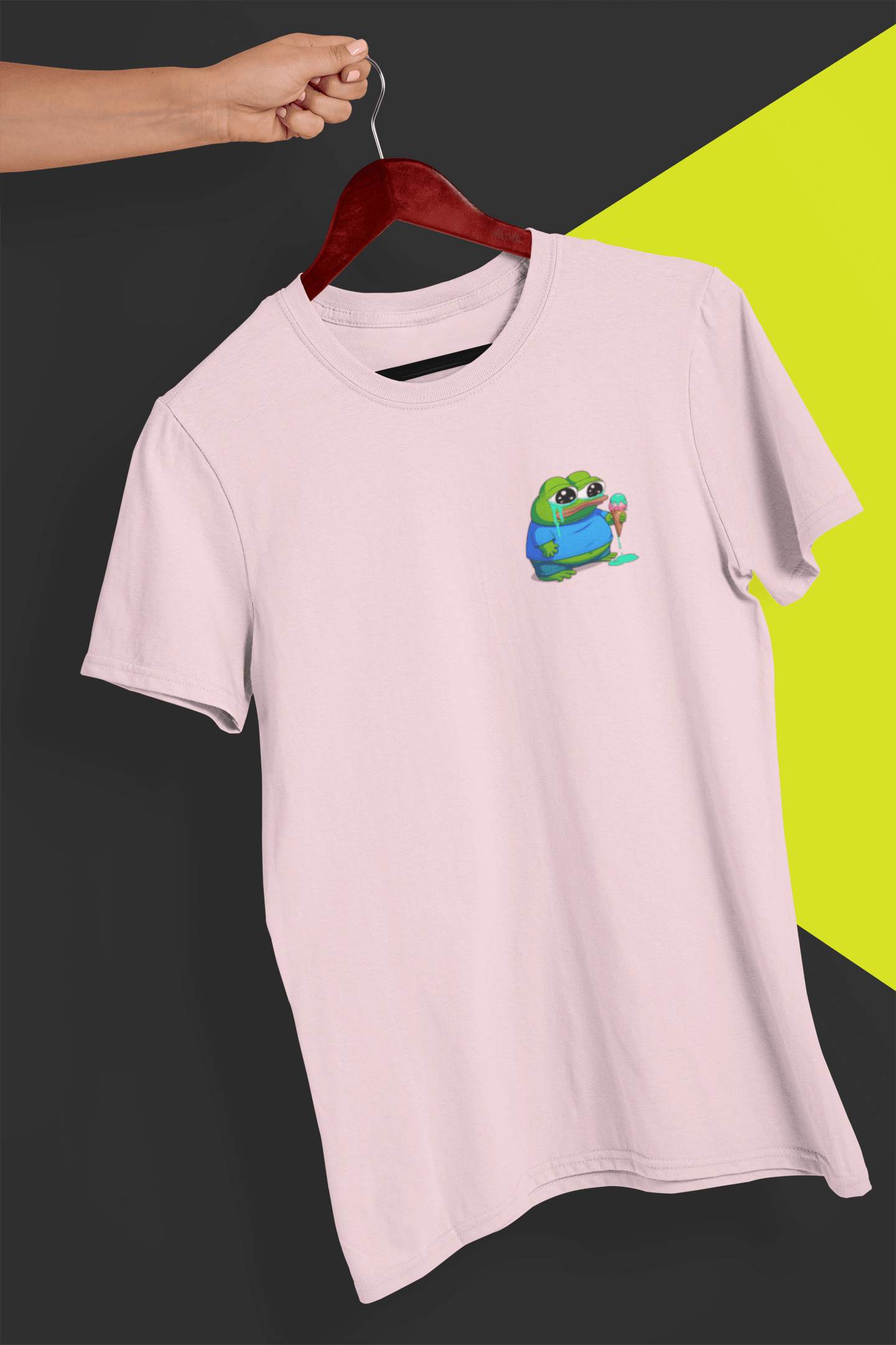 A pink T-shirt with a small cute apu apustaja pepe in the right corner, held by a hand against a split black and yellow background.