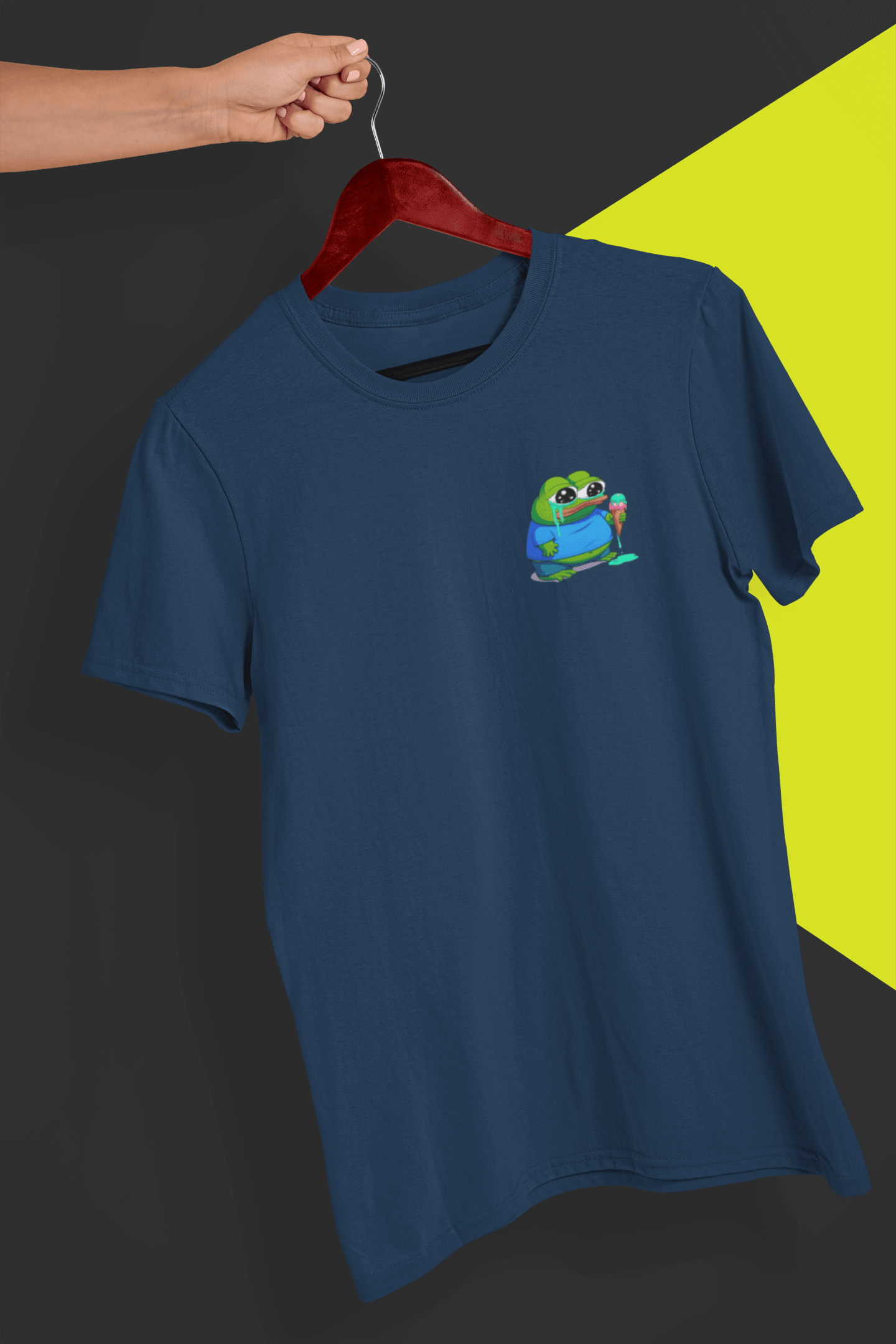 A navy blue T-shirt with a small cute apu apustaja pepe in the right corner, held by a hand against a split black and yellow background.