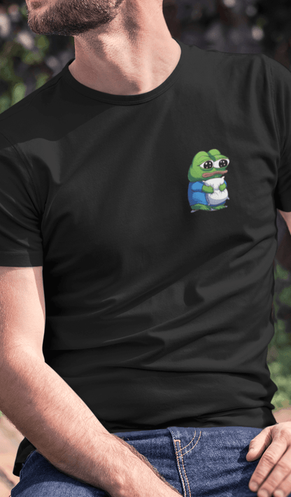 A man wears a black T-shirt featuring a cute apu apustaja pepe in the corner hugging a pillow.