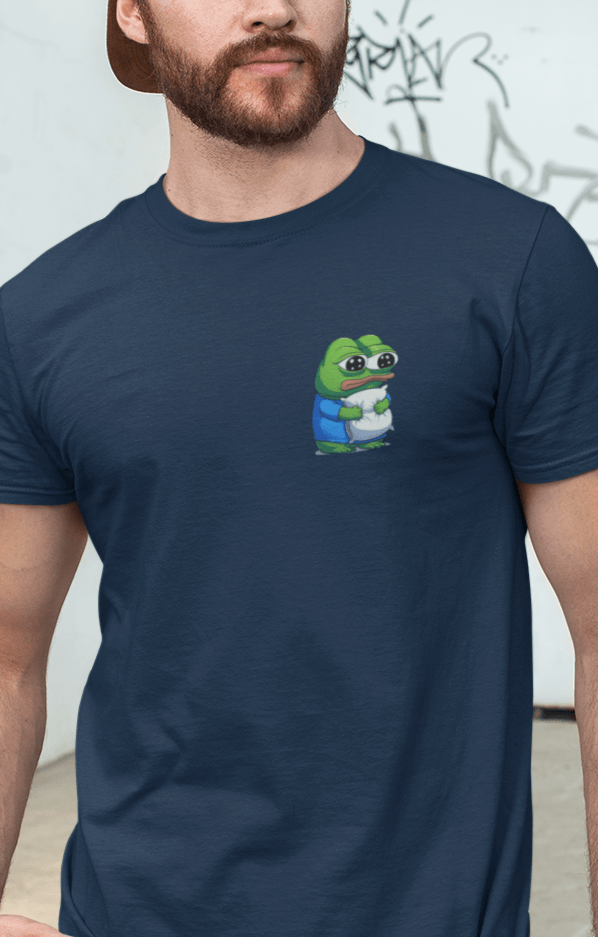 A man wears a navy-blue T-shirt featuring a cute apu apustaja pepe in the corner hugging a pillow.