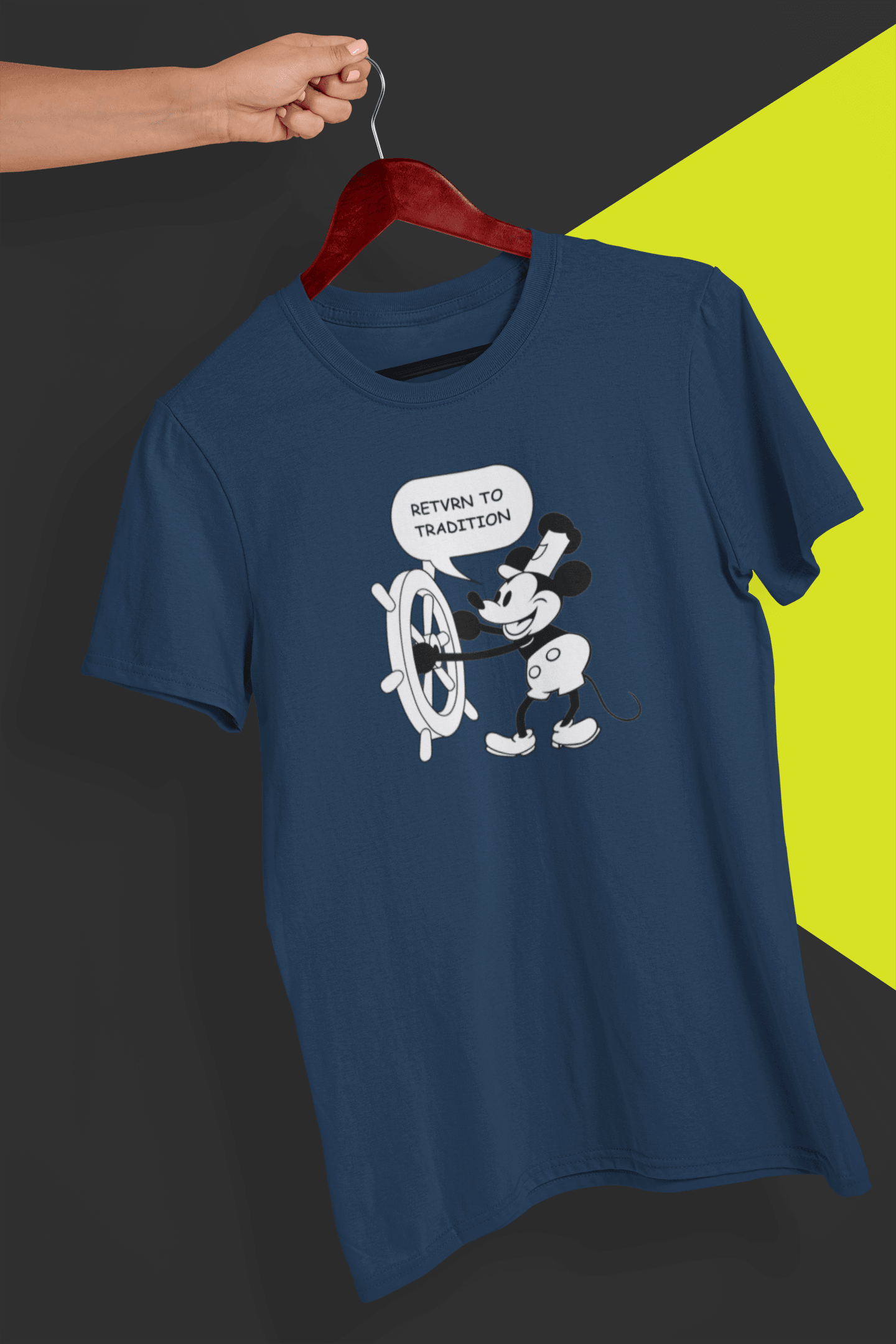 A navy T-shirt with a cute retro Mickey Mouse (Willy) driving a steamboat in the middle, saying &quot;Return to tradition&quot;, held by a hand against a split black and yellow background.