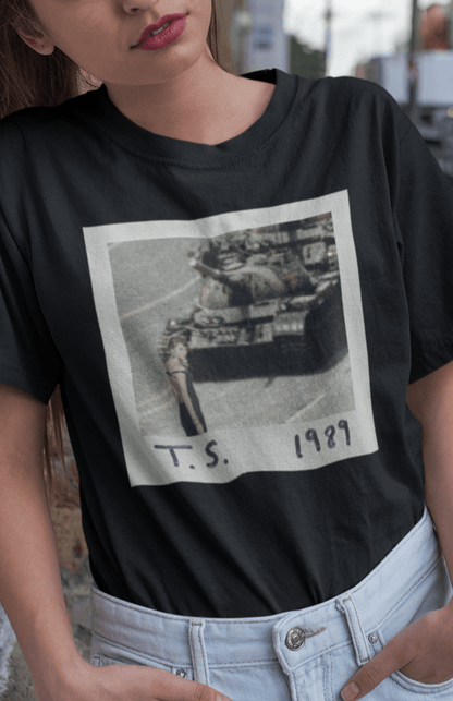 A woman wearing a black T-shirt with Taylor Swift in front of a tank written &quot;T.S. 1989&quot;.