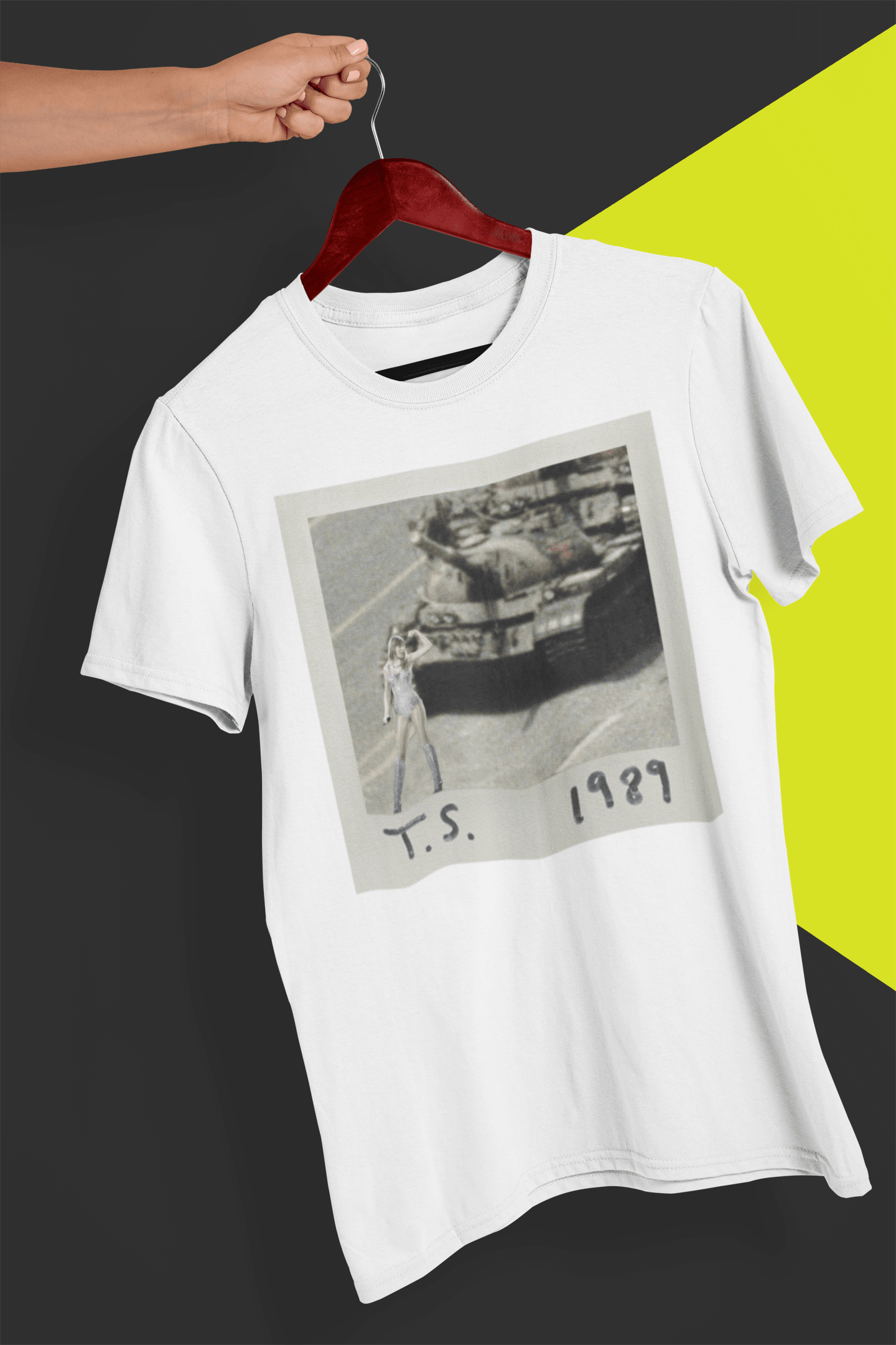 A white T-shirt with Taylor Swift in front of a tank written &quot;T.S. 1989&quot;, held by a hand against a split black and yellow background.