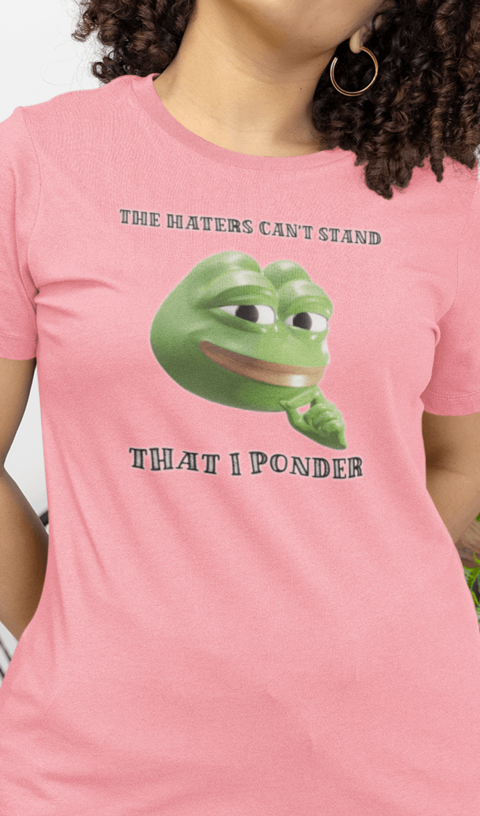 A woman wears a pink T-shirt featuring a funny 3d smug pepe in the middle, saying &quot;The haters cant&#39;s stand that I ponder&quot;.