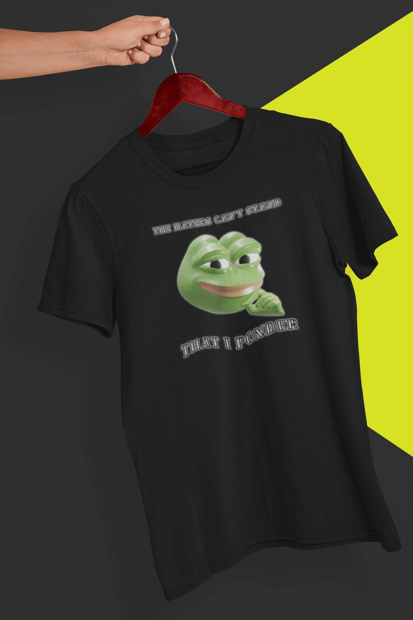 A black T-shirt with a funny 3d smug pepe in the middle, saying &quot;The haters cant&#39;s stand that I ponder&quot;, held by a hand against a split black and yellow background.