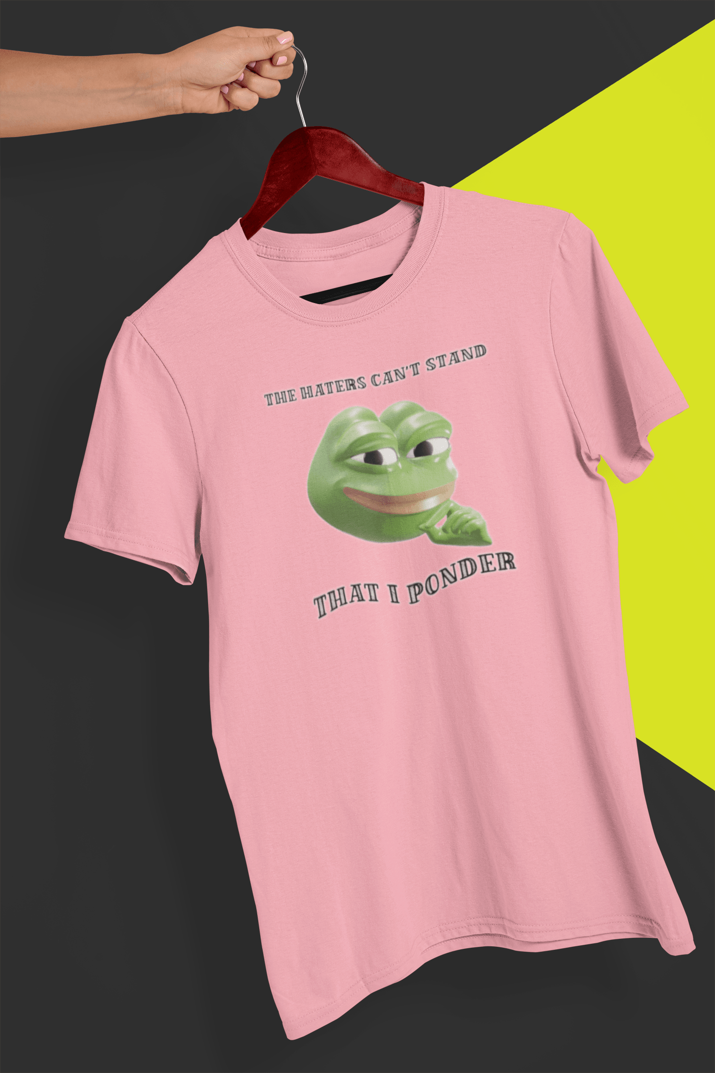 A pink T-shirt with a funny 3d smug pepe in the middle, saying &quot;The haters cant&#39;s stand that I ponder&quot;, held by a hand against a split black and yellow background.