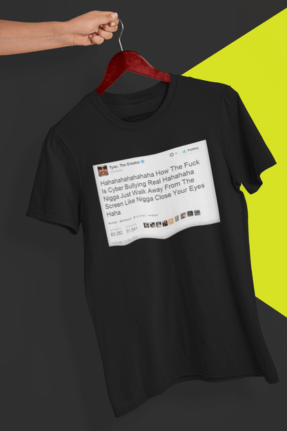 A black T-shirt with a Tyler The Creator Tweet written &quot;Hahaha How The F*ck Is Cyber Bullying Real Haha N*gga Just Walk Away From The Screen, Like, N*gga Close Your Eyes Haha&quot;, held by a hand against a split black and yellow background.