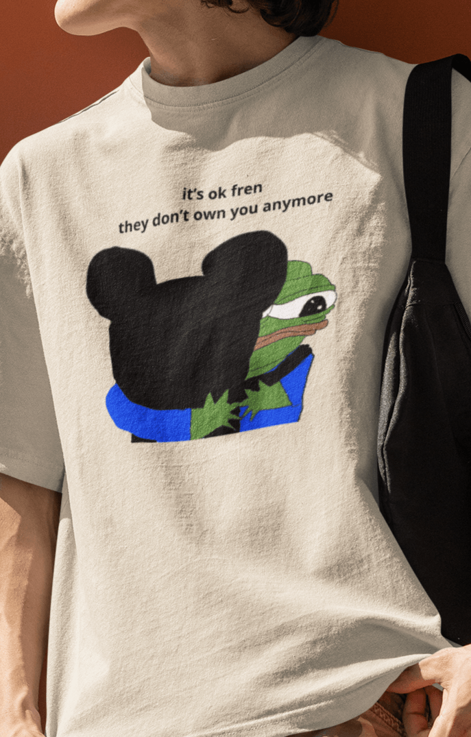 A man wears an off-white T-shirt featuring Mickey Mouse hugging a cute Apu in the middle, saying &quot;it&#39;s ok fren, they don&#39;t own you anymore&quot;.