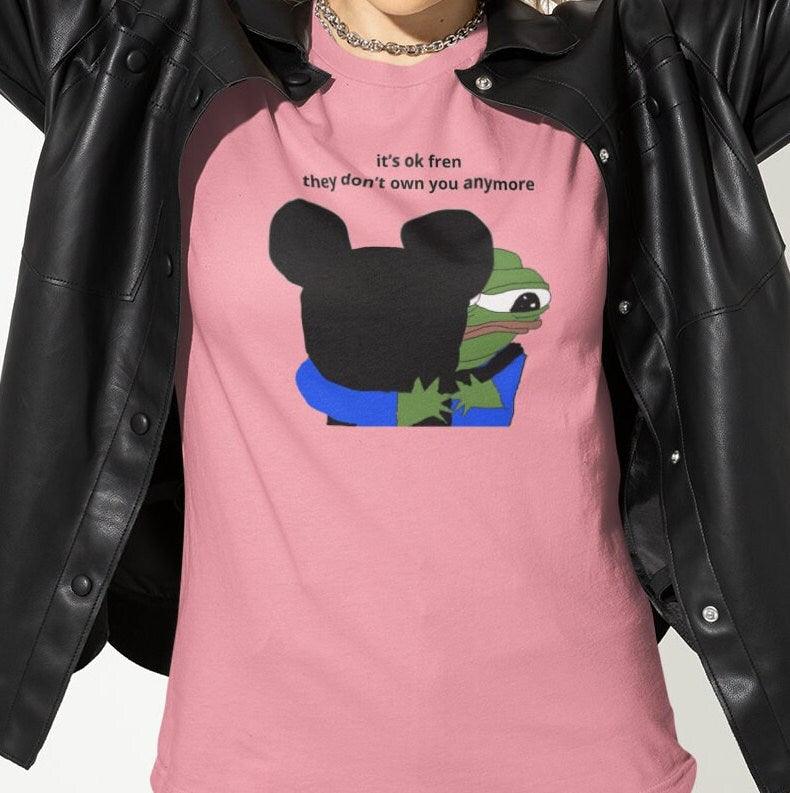 A woman wears a pink T-shirt featuring Mickey Mouse hugging a cute Apu in the middle, saying &quot;it&#39;s ok fren, they don&#39;t own you anymore&quot;.