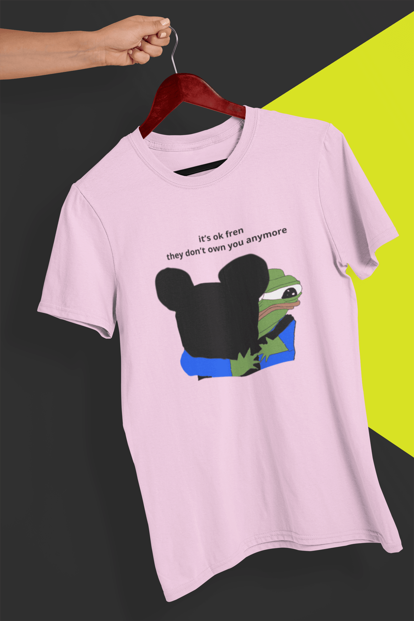 A pink T-shirt with Mickey Mouse hugging a cute Apu in the middle, saying &quot;it&#39;s ok fren, they don&#39;t own you anymore&quot;, held by a hand against a split black and yellow background.