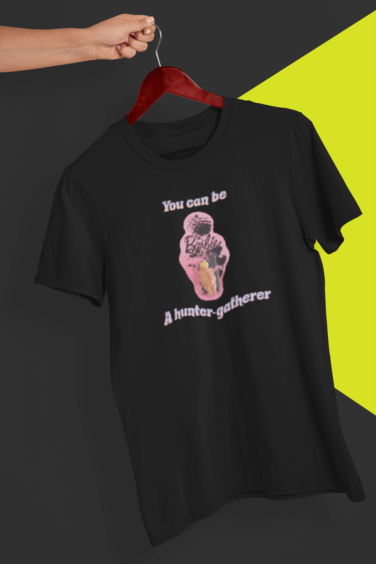 A black T-shirt featuring the venus impudique that says &quot;Barbie You can be a hunter-gatherer&quot;, held by a hand against a split black and yellow background.